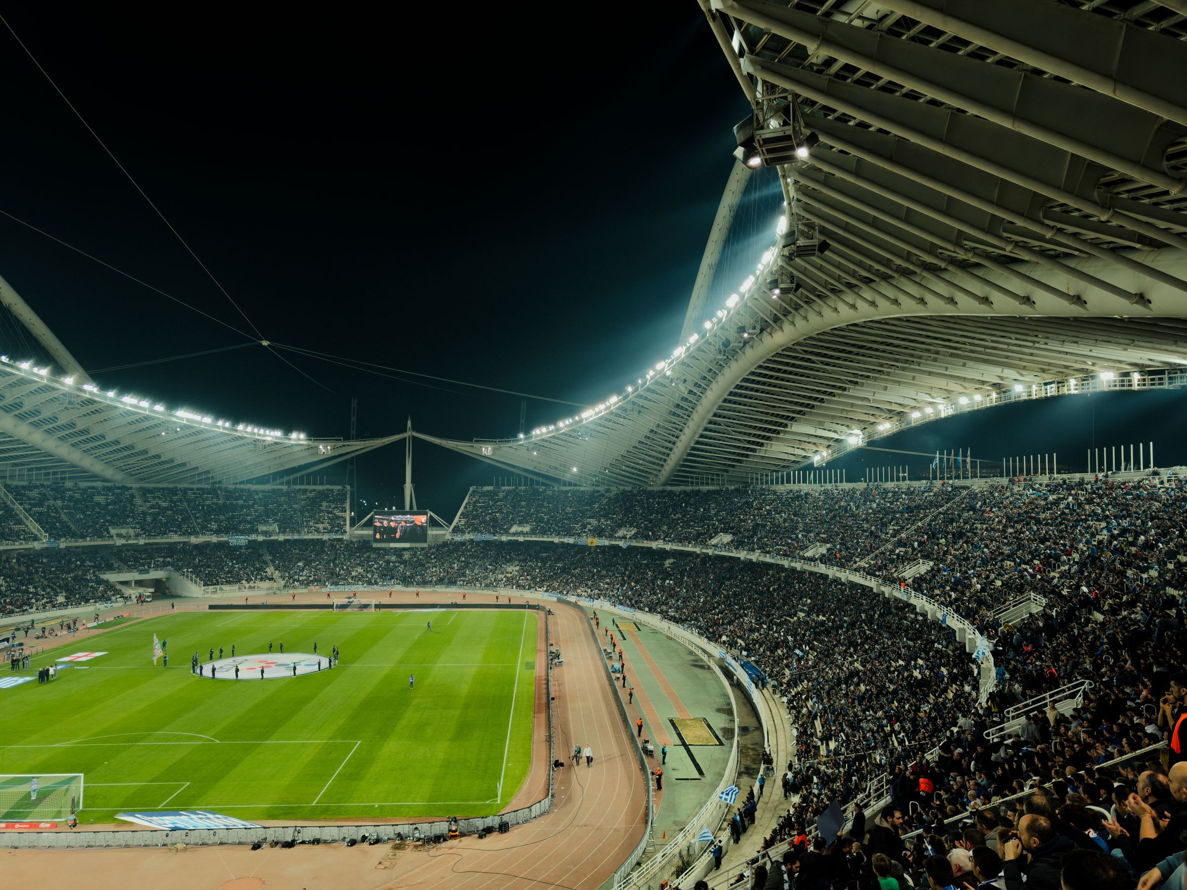 Estadio de fútbol abarrotado de noche bajo los focos, con la afición llenando las gradas