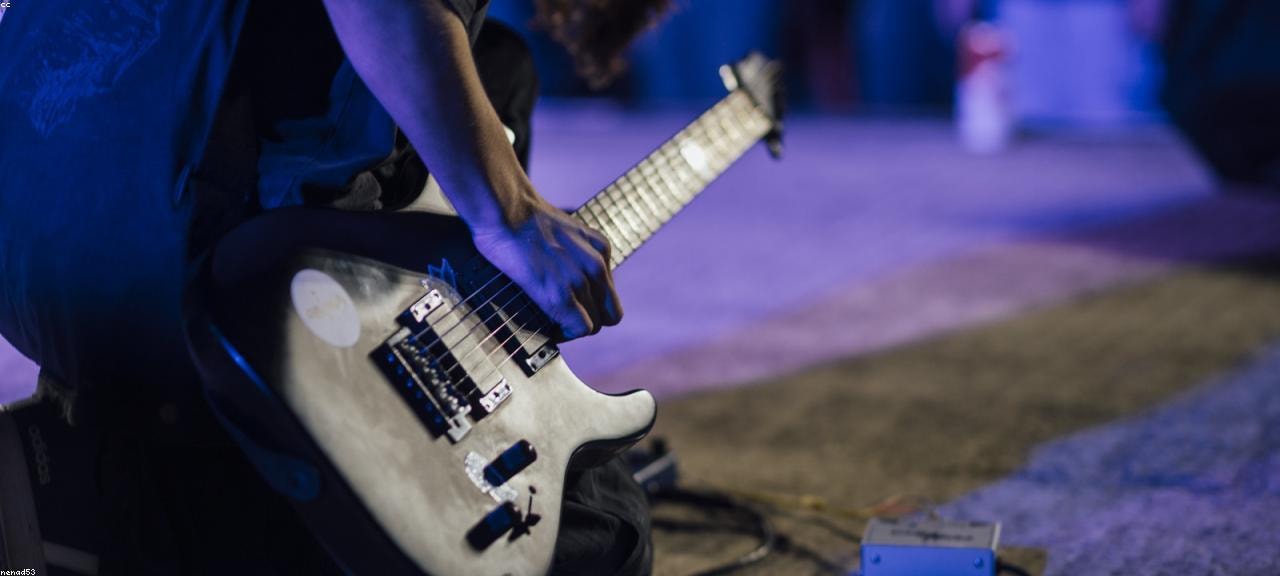 Primer plano de un guitarrista tocando la guitarra eléctrica en un escenario con luces azules