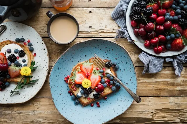 Desayuno visto desde arriba: tostadas con frutos rojos, café con leche y un bol de cerezas