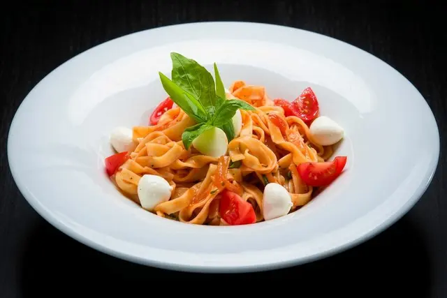 Plato blanco de tallarines con salsa de tomate, tomates cherry, mozzarella y albahaca fresca