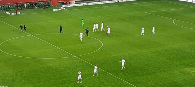 Des footballeurs en blanc entrent sur la pelouse d'un stade, vus depuis les tribunes