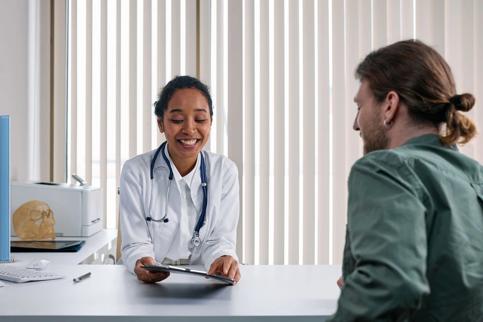 Una médica sonriente con bata blanca muestra un informe a un paciente en su consulta